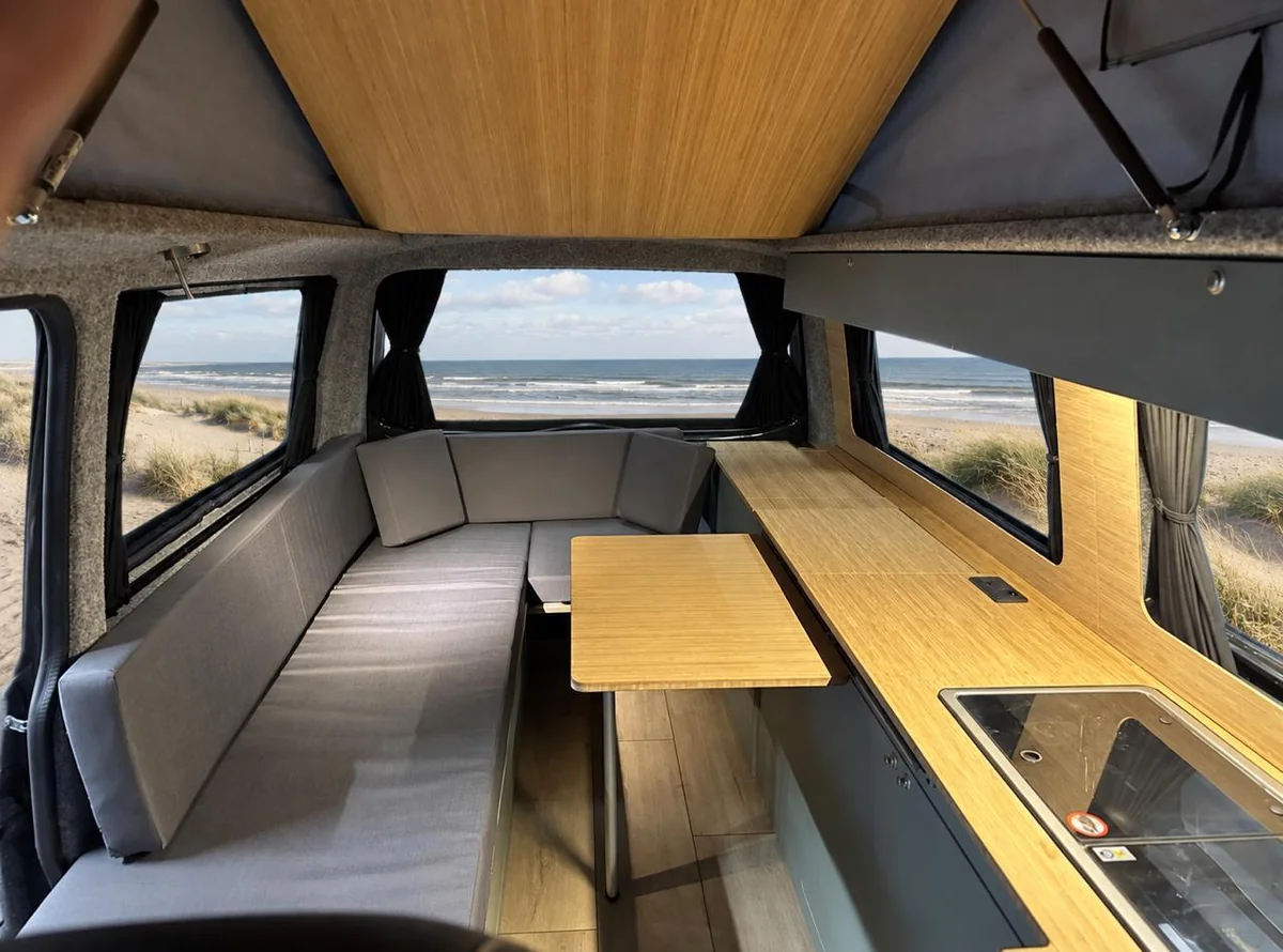 Grijze zitbank, houten tafel en keuken in een camper met uitzicht op zee